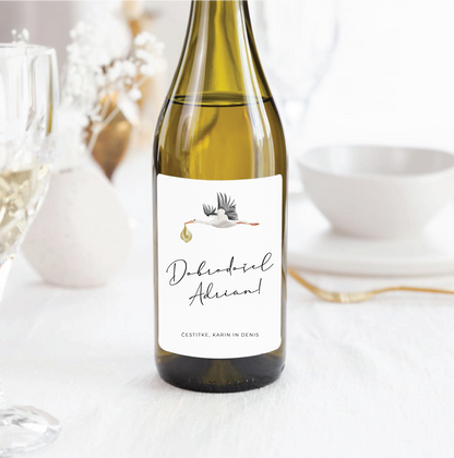 Personalizirana vinska etiketa s štorkljo in napisom »Dobrodošel Adrian« na steklenici belega vina.