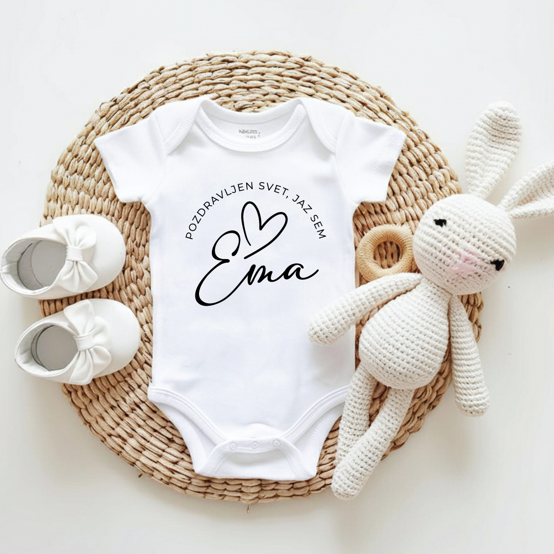 Beli personaliziran bodi za dojenčka z napisom Pozdravljen svet in imenom Ema, ob njem plišast zajček in otroški copatki.
