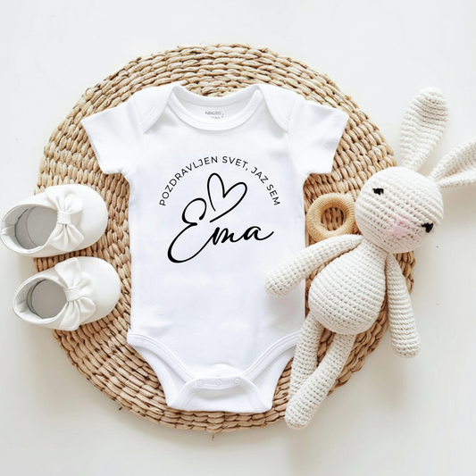 Beli personaliziran bodi za dojenčka z napisom Pozdravljen svet in imenom Ema, ob njem plišast zajček in otroški copatki.